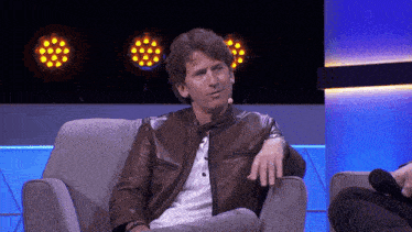 a man wearing a brown leather jacket sits in a chair