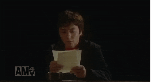 a man sits in a chair reading a piece of paper with amv on the bottom right