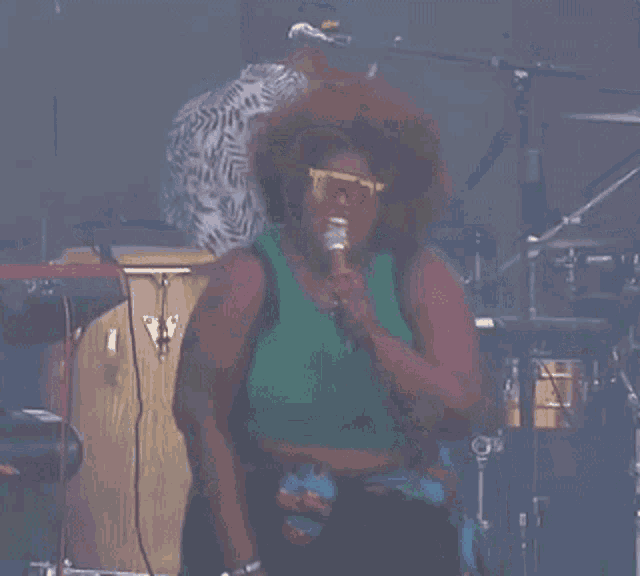 a woman singing into a microphone with a man playing drums in the background