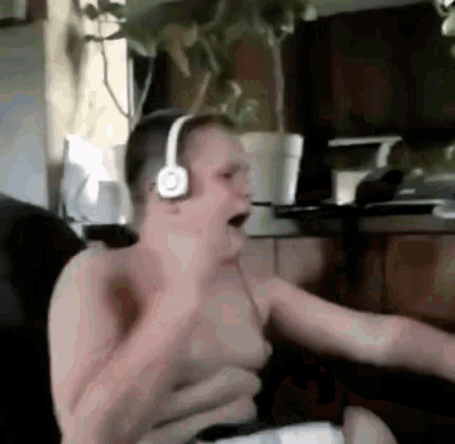a shirtless man wearing headphones is sitting in a chair and playing a video game .