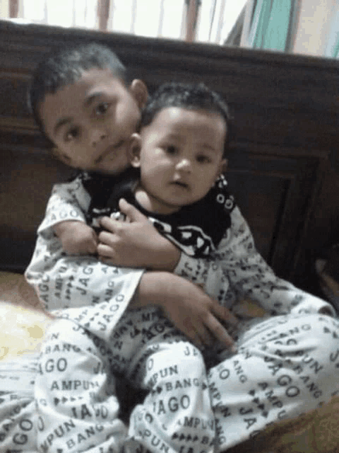 a boy is holding a baby wearing pajamas that say jago on them