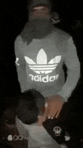a man wearing a mask and an adidas sweater is standing in the dark .