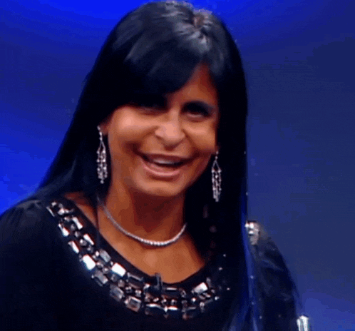 a woman wearing a necklace and earrings laughs with her mouth open