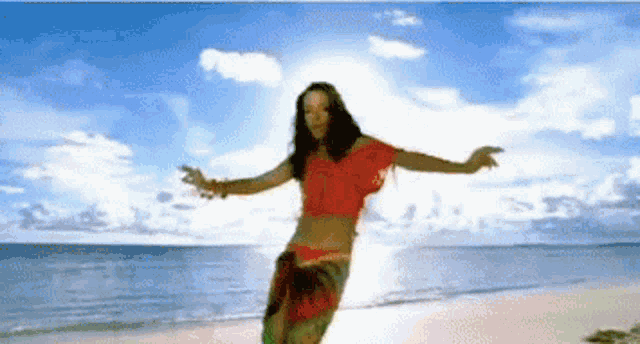 a woman in a red top is dancing on the beach with her arms outstretched