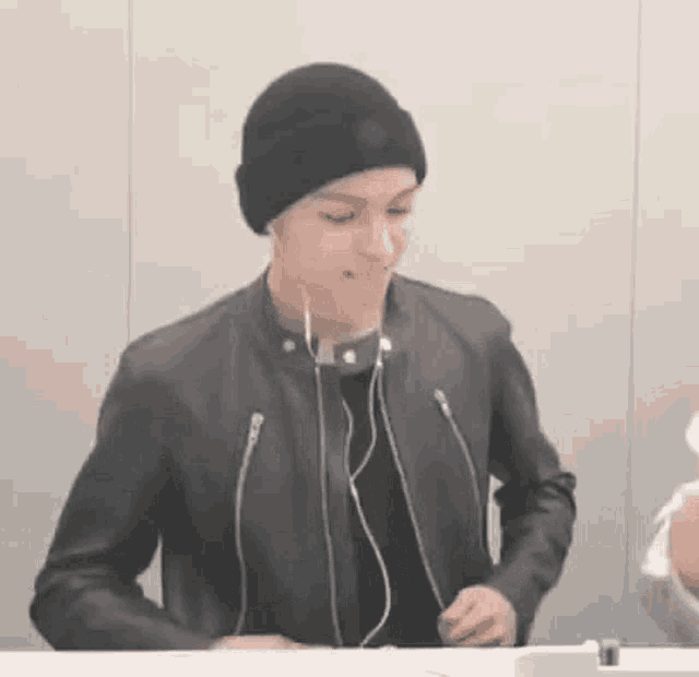 a man wearing a beanie and a leather jacket is sitting at a table with headphones on .