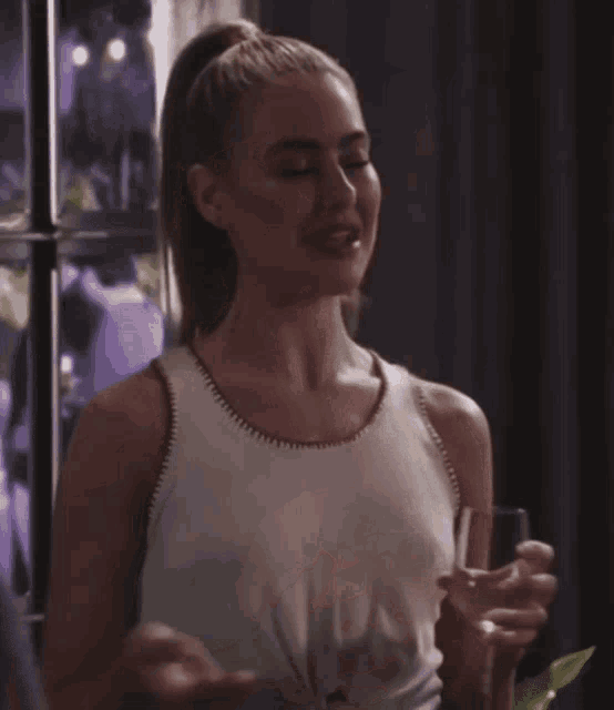 a woman in a white tank top is holding a glass of wine and smiling