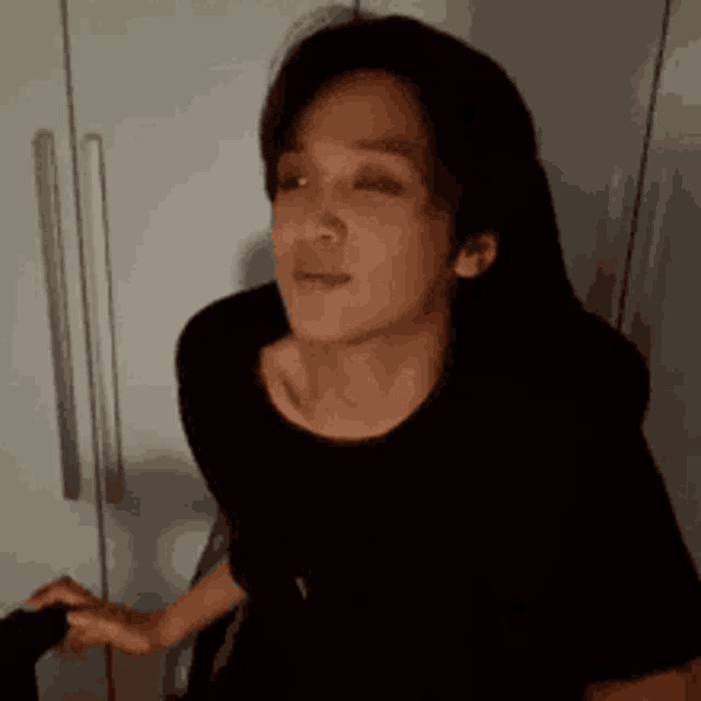 a woman in a black shirt is making a funny face while standing in front of a refrigerator .
