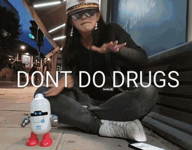 a woman wearing a hurley shirt sits on the sidewalk with a robot