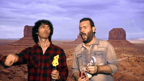 a man in a plaid shirt holds a guitar in front of a desert landscape