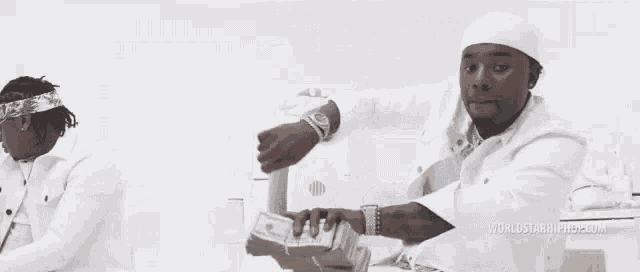 a man in a white hat is holding a stack of money in his hand .