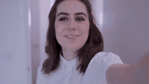 a woman in a white shirt is taking a selfie with her cell phone .