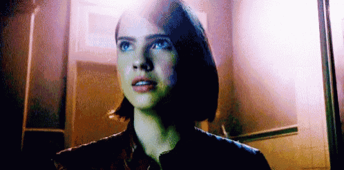 a woman with blue eyes is standing in a dark room looking up .