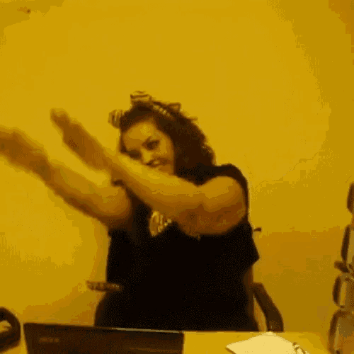 a woman sitting at a desk with her arms in the air wearing a black shirt that says ' reebok ' on it