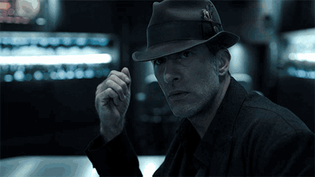a man wearing a fedora and a black jacket is pointing