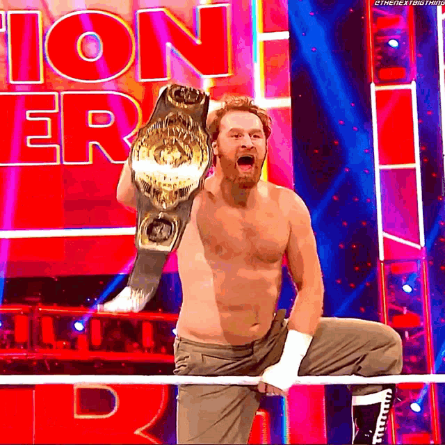 a shirtless wrestler is holding a championship belt in front of a sign that says ' tion '