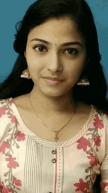 a woman wearing a necklace and earrings looks at the camera with a blue background