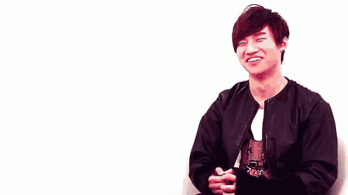 a young man is sitting in front of a white wall and smiling .