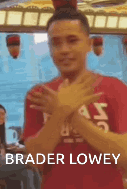 a man in a red shirt is making a x with his hands and the words brader lowey below him .