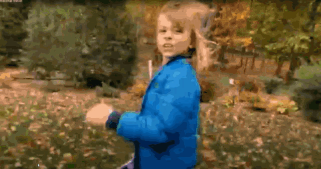 a little girl in a blue jacket is running through a field of leaves