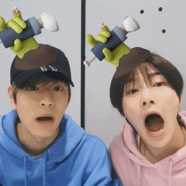 a couple of boys are standing next to each other with their mouths open and one has a toy on his head .