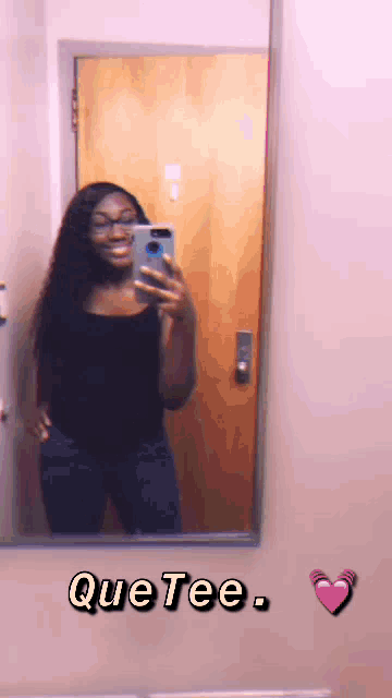 a woman taking a selfie in front of a mirror with que tee written on the bottom right