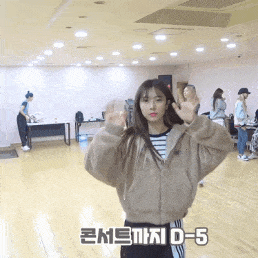 a girl in a tan jacket stands in a room with the numbers d-5 written on the floor