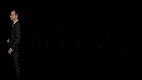 a man in a suit and tie is standing with his hands on his hips in a dark room .