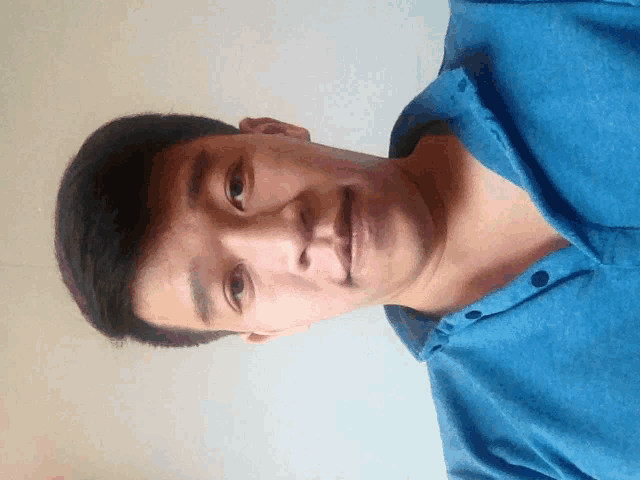 a young man wearing a blue shirt looks at the camera