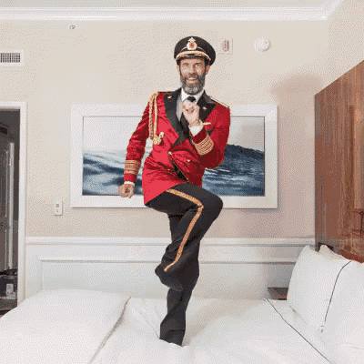 a man in a red jacket and black pants jumps on a bed