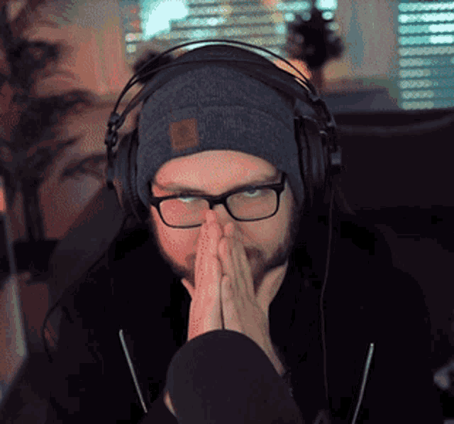 a man wearing headphones and a beanie holds his hands together