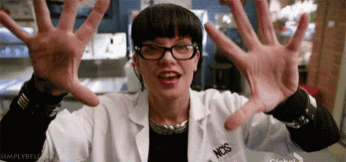 a woman wearing glasses and a lab coat is making a funny face with her hands in the air .