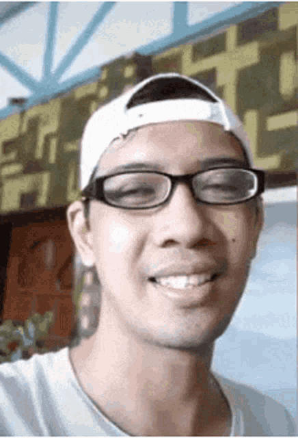 a man wearing glasses and a white baseball cap is smiling for the camera .