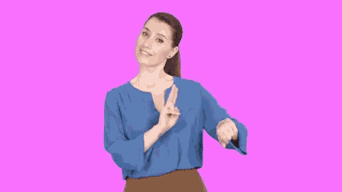 a woman wearing a blue shirt and brown pants is pointing at her watch .