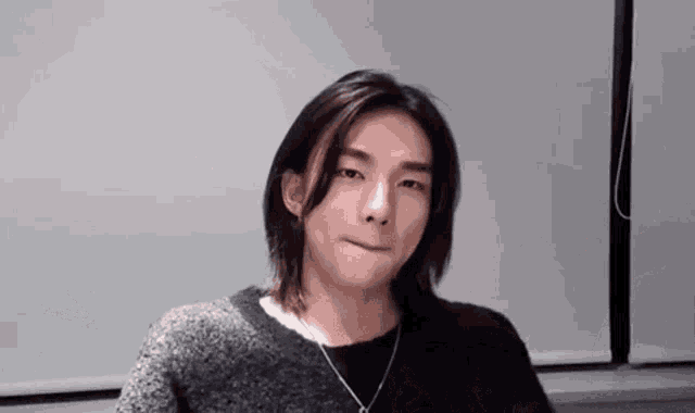a young man with long hair is making a funny face while wearing a black sweater and a necklace .