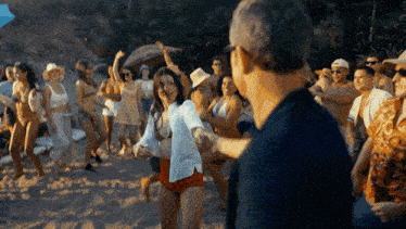 a group of people are dancing on a beach and one of them is wearing a shirt that says ' sydney ' on it