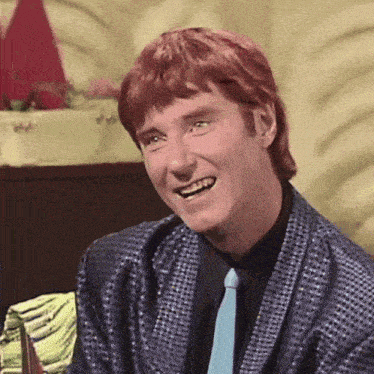 a man with red hair is smiling and wearing a blue jacket and tie .