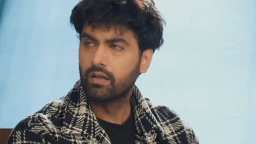 a man with a beard is wearing a plaid shirt and a black shirt .