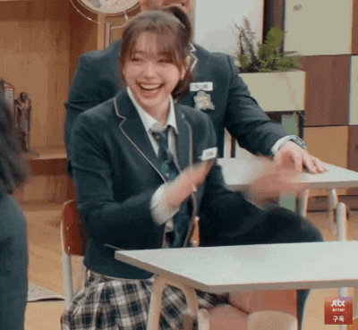 a girl in a school uniform is sitting at a desk with a man in a suit