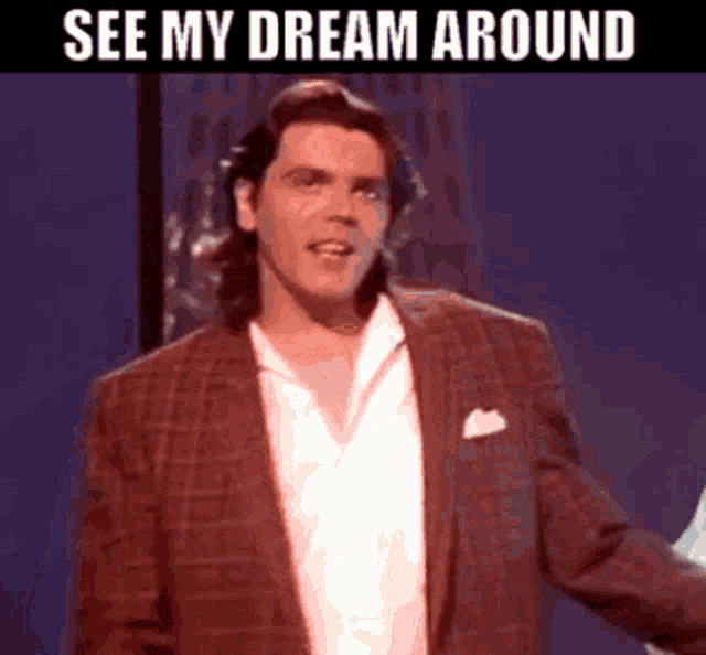 a man in a suit and white shirt is standing in front of a sign that says see my dream around