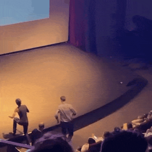 a group of people are sitting in an auditorium watching a presentation on a stage