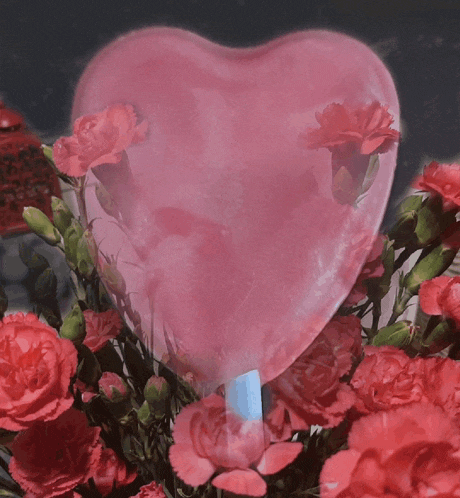 a pink heart shaped balloon is surrounded by red flowers