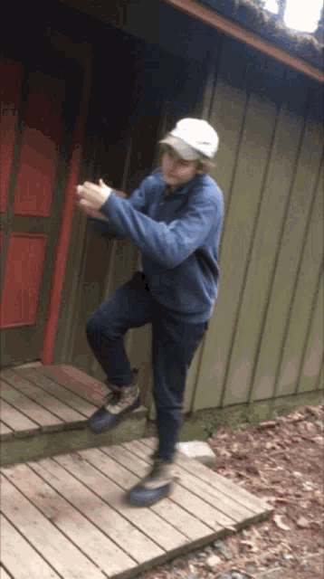a man wearing a blue sweater and a white hat stands on a wooden deck