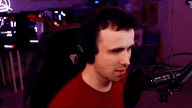 a man in a red shirt is sitting in a chair in front of a microphone .