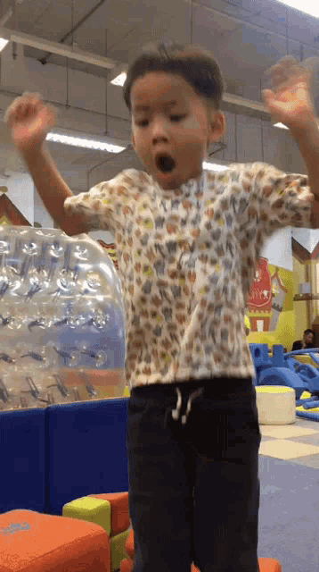a young boy in a leopard print shirt is jumping in the air with his arms outstretched