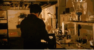 a man is standing in a lab with a microscope and bottles on a counter