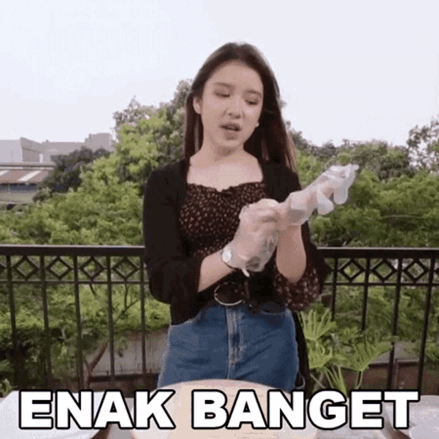 a woman wearing gloves is standing on a balcony with the words enak banget written above her .