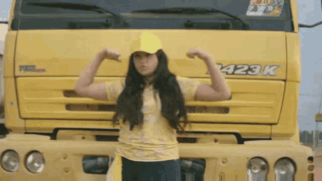 a girl is flexing her muscles in front of a yellow truck with the number 429k on it