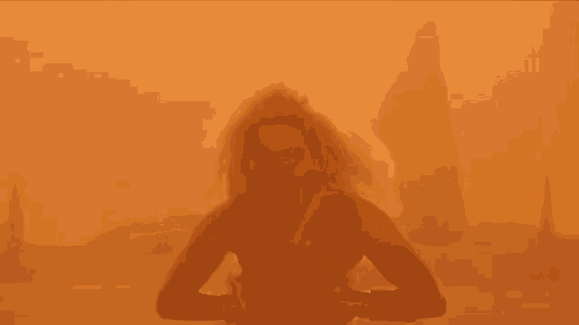 a woman is standing in a desert with her arms outstretched in front of a city .