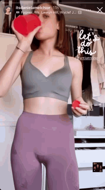 a woman in a gray sports bra and purple leggings holds a red heart in her hand ..