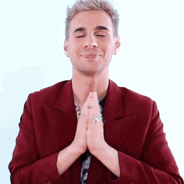 a man wearing a red jacket is praying with his hands together